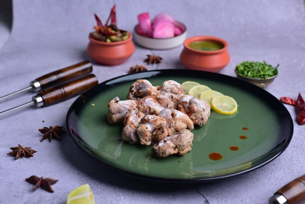 A close-up of a sizzling plate of chicken tikka, garnished with fresh herbs and lemon wedges.