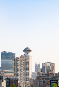 A skyline featuring a variety of buildings, including a notable tower with a round, futuristic top. The architecture ranges from modern high-rises to older, more traditional structures. The clear blue sky serves as the backdrop, adding a sense of openness and space.
