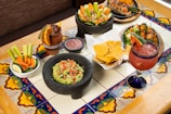 Close-up of colorful healthy Mexican snacks arranged on rustic wooden table with green leaves.
