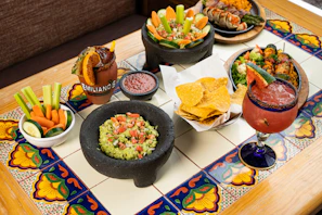 A festive table set outdoors with bright papel picado banners and bowls of guacamole and chips.