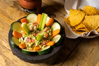 Close-up of a colorful bowl of guacamole topped with diced tomatoes and a sprinkle of chili flakes, presented on a rustic wooden table.