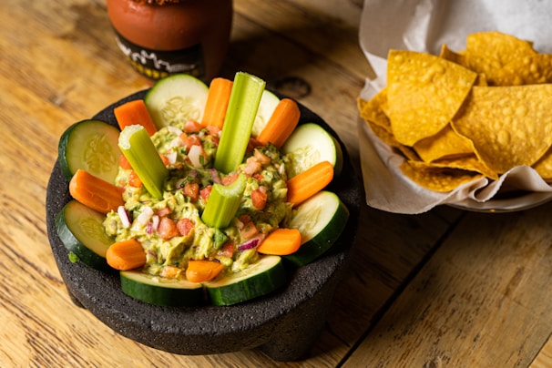 Close-up of a colorful bowl of guacamole topped with diced tomatoes and a sprinkle of chili flakes, presented on a rustic wooden table.