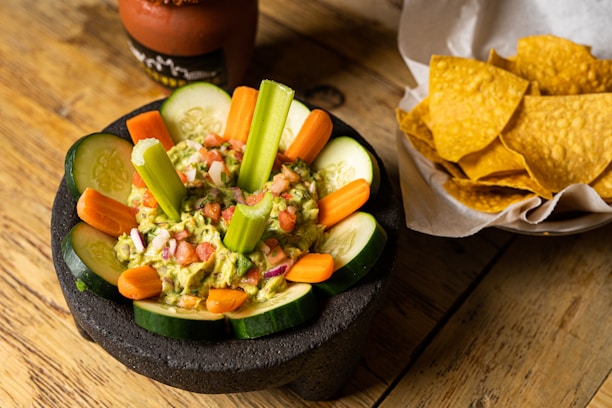 A vibrant bowl of fresh guacamole surrounded by colorful tortilla chips on a rustic wooden table.