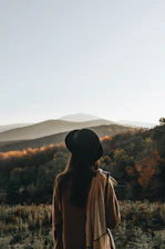 a woman standing in a field with mountains in the background