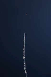 A sleek rocket launching into a clear blue sky, leaving a trail of white smoke.
