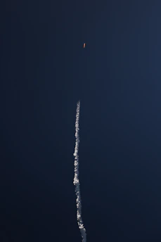 A sleek rocket launching into a clear blue sky, leaving a trail of white smoke.