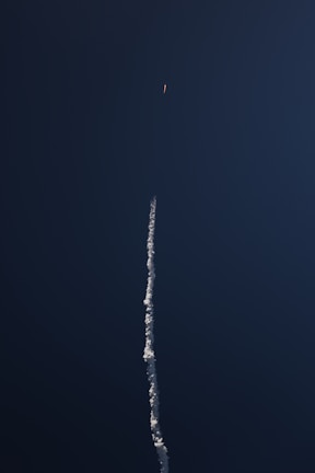 A launch vehicle ascending into a clear blue sky, leaving a trail of smoke
