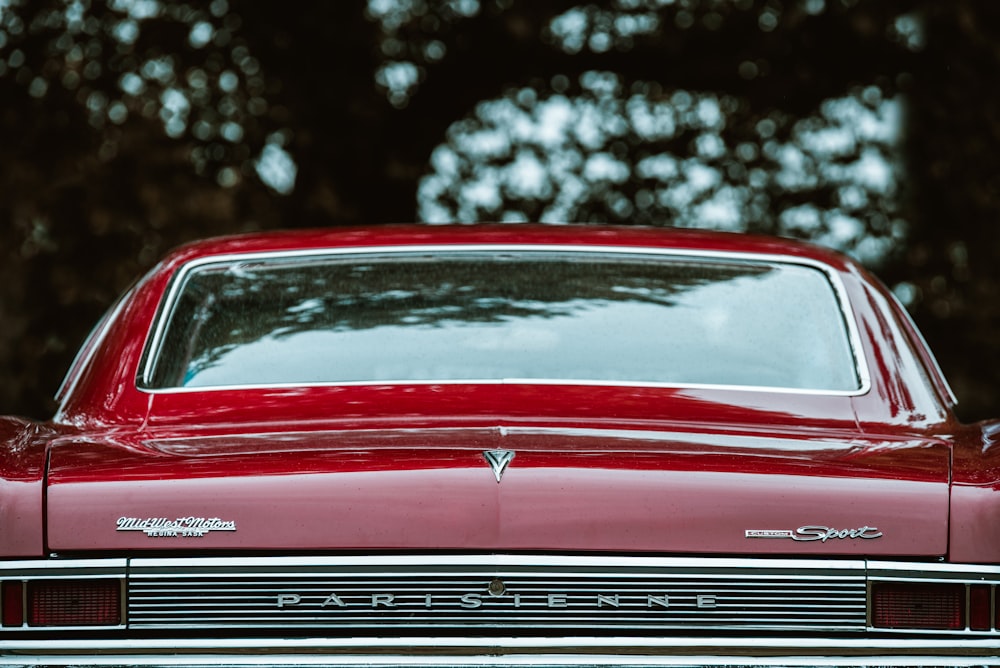 a red classic car parked in front of a tree