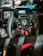 A close-up view of a high-tech racing car steering wheel with multiple buttons and controls. The dashboard features digital displays, and the steering wheel is made of carbon fiber, suggesting its use in a professional racing environment.