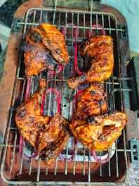 A close-up of a juicy, perfectly grilled BBQ chicken with char marks, served on a rustic wooden platter with fresh herbs.