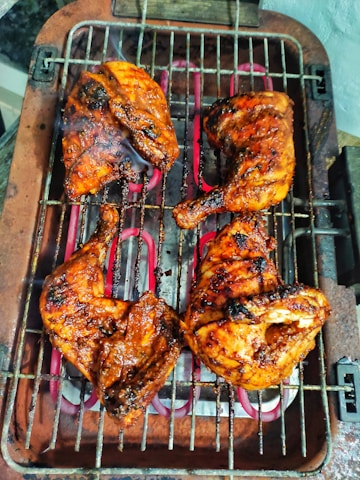 A close-up of a juicy, perfectly grilled BBQ chicken with char marks, served on a rustic wooden platter with fresh herbs.