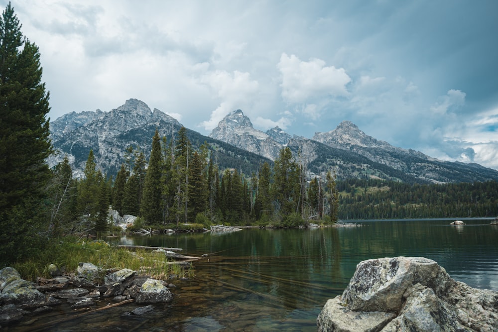 a lake surrounded by trees and mountains under a cloudy sky