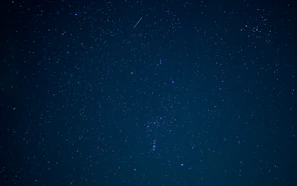 A serene night sky with shooting stars and subtle astrological symbols overlay
