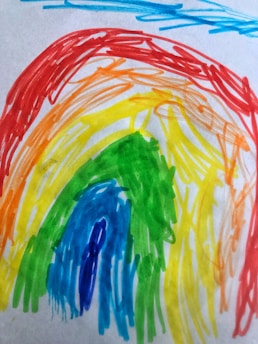 A colorful rainbow drawing in a childlike, sketchy style with arcs in red, orange, yellow, green, blue, and purple. Background shows a few scattered light blue lines.