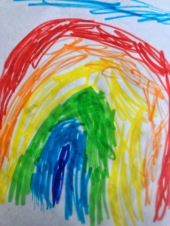 A child holding a colorful rainbow drawing in a hospital room filled with soft blue and white tones.