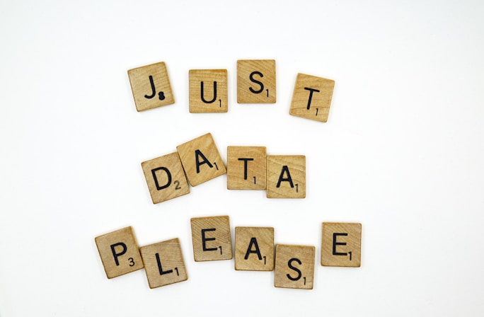 Wooden letter tiles resembling those from a word game are arranged to spell out the phrase 'JUST DATA PLEASE' on a plain white background. The tiles have black letters and numbers indicating point values.