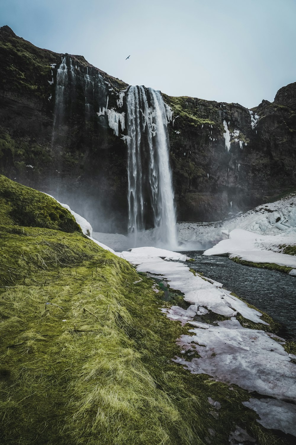 a waterfall with snow on the ground and grass on the ground