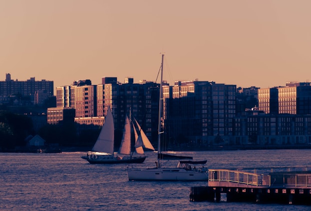 A cozy sailboat gliding on the Tagus River at sunset, with Lisbon’s iconic skyline glowing warmly in the background.