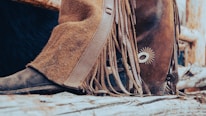 Close-up of equestrian boots and gloves resting on a rustic wooden fence.
