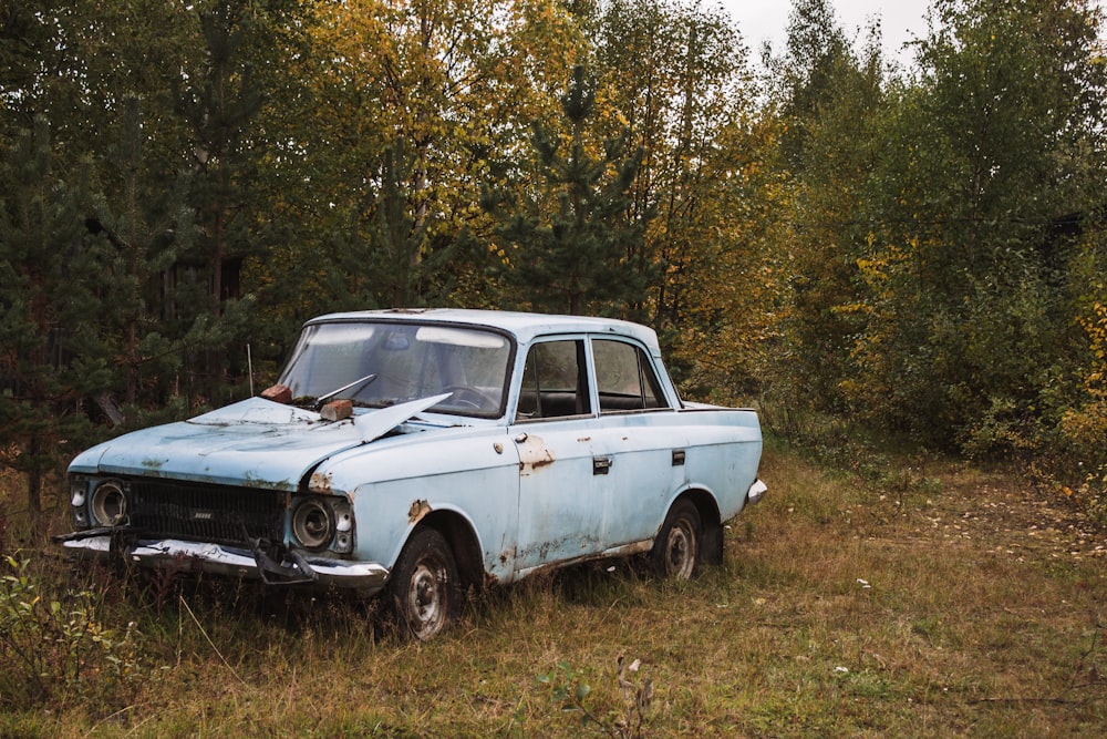 an old blue car is parked in a field