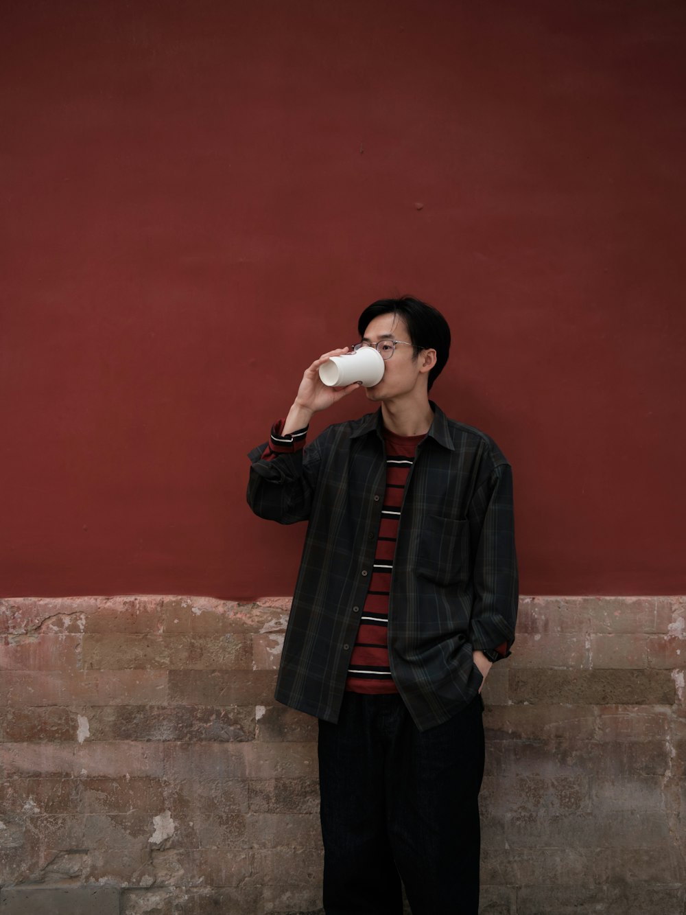 a man standing next to a red wall drinking from a cup