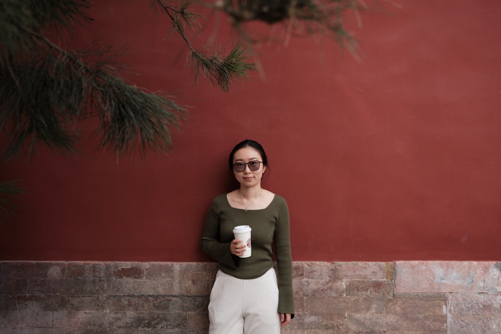a woman leaning against a wall with a cup of coffee