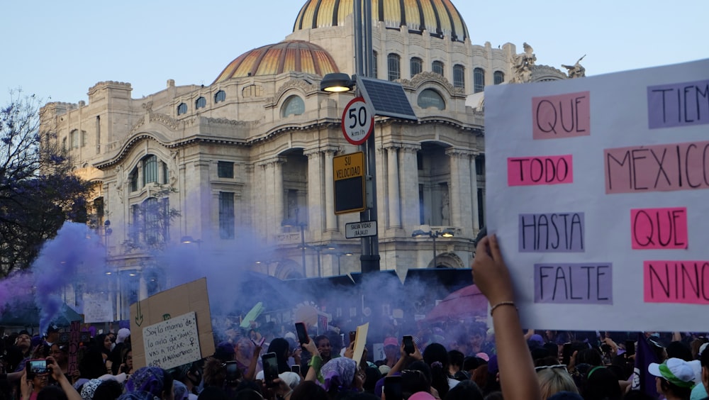 a crowd of people holding signs and smoke in front of a building