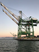 A large crane being carefully loaded onto a cargo ship at a busy port.