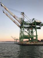 A modern cargo crane lifting heavy containers at sunset in Khorfakkan port.