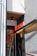 A small entrance to a building features a neon red 'SAUNA' sign above the door. The wall is textured and painted gray, with a smooth white section on top, and there is a black, ceiling-mounted light fixture. The door itself is glass with red circular designs and reflections visible.