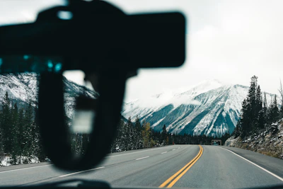 A scenic mountain road viewed from the driver's seat, with a glimpse of a travel sport sling bag on the passenger seat.