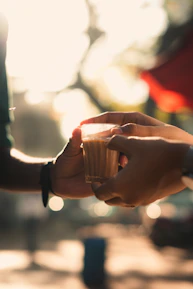 Close-up of hands exchanging a book and a cup of tea, symbolizing connection through art.