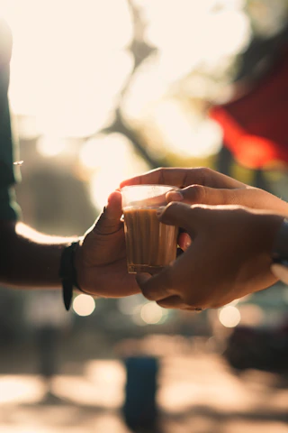 Close-up of hands exchanging a book and a cup of tea, symbolizing connection through art.