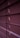 Horizontal window blinds are shown in a dimly lit setting with subtle gradients of purple and pink tones. Light peeks through the small openings between the slats.