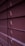Horizontal window blinds are shown in a dimly lit setting with subtle gradients of purple and pink tones. Light peeks through the small openings between the slats.