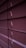 Horizontal window blinds are shown in a dimly lit setting with subtle gradients of purple and pink tones. Light peeks through the small openings between the slats.