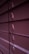 Horizontal window blinds are shown in a dimly lit setting with subtle gradients of purple and pink tones. Light peeks through the small openings between the slats.
