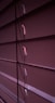 Horizontal window blinds are shown in a dimly lit setting with subtle gradients of purple and pink tones. Light peeks through the small openings between the slats.