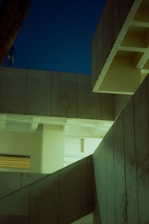 Angular concrete architecture with geometric lines and patterns is highlighted under soft artificial lighting against a twilight sky.