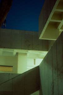 Angular concrete architecture with geometric lines and patterns is highlighted under soft artificial lighting against a twilight sky.