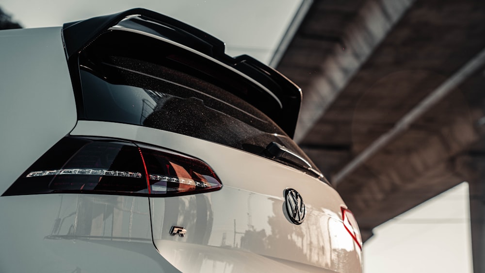 the back end of a white car with a bridge in the background