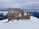 A wooden sign in snowy mountains with the words 'Back to the Wild' carved into it. The background features snow-capped peaks under a cloudy sky.