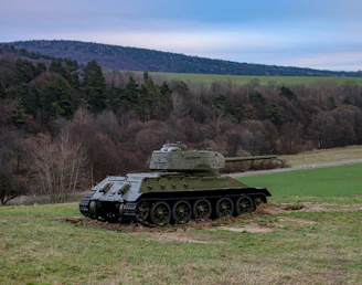 A vintage World War II tank moving through a muddy battlefield under a cloudy sky.