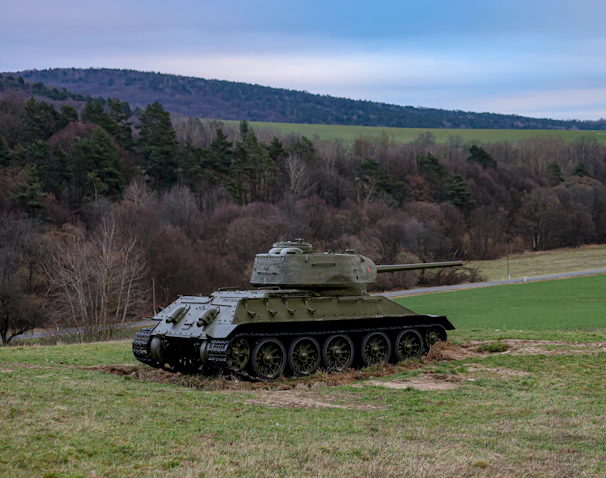 A vintage World War II tank moving through a muddy battlefield under a cloudy sky.