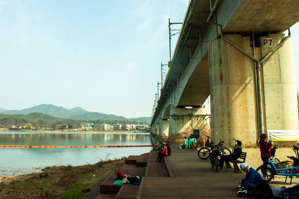 a group of people sitting under a bridge next to a body of water