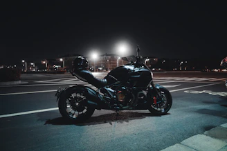 A sleek black motorcycle parked under dim street lights at night.