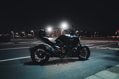 A sleek black motorcycle parked under dim street lights at night.