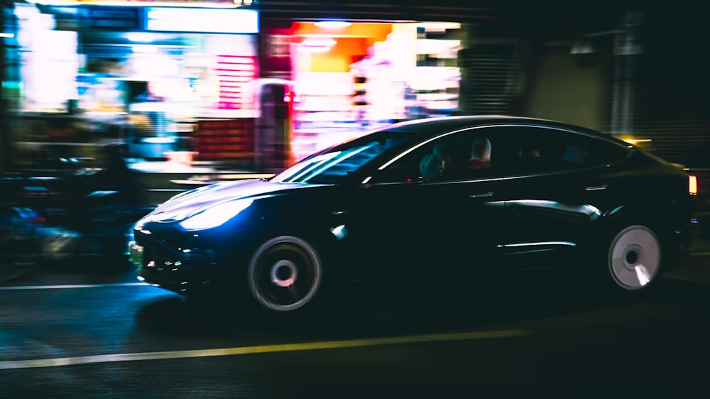 a black car driving down a street at night