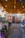 A rustic outdoor space adorned with hanging lights, colorful decorative fabrics and pots. Wooden beams support the ceiling, and a variety of vibrant crafts and plants are displayed throughout. The setting feels cozy and inviting, with a mix of natural elements and artisanal goods.