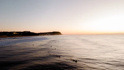 A serene beach at dusk with surfers catching waves near Weligama shore.